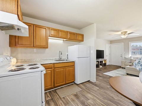 A kitchen with a white stove top oven and a white refrigerator with wooden cabinets.