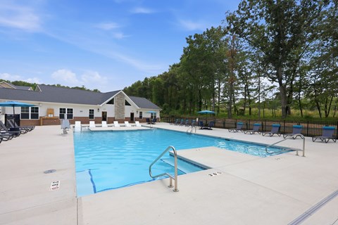 A large outdoor swimming pool with a diving board and a building in the background.