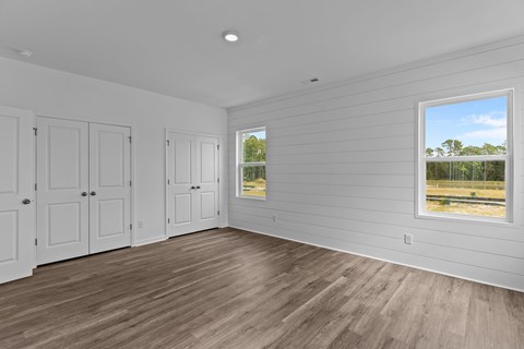 A room with white walls and wooden flooring with a window showing a view of trees.