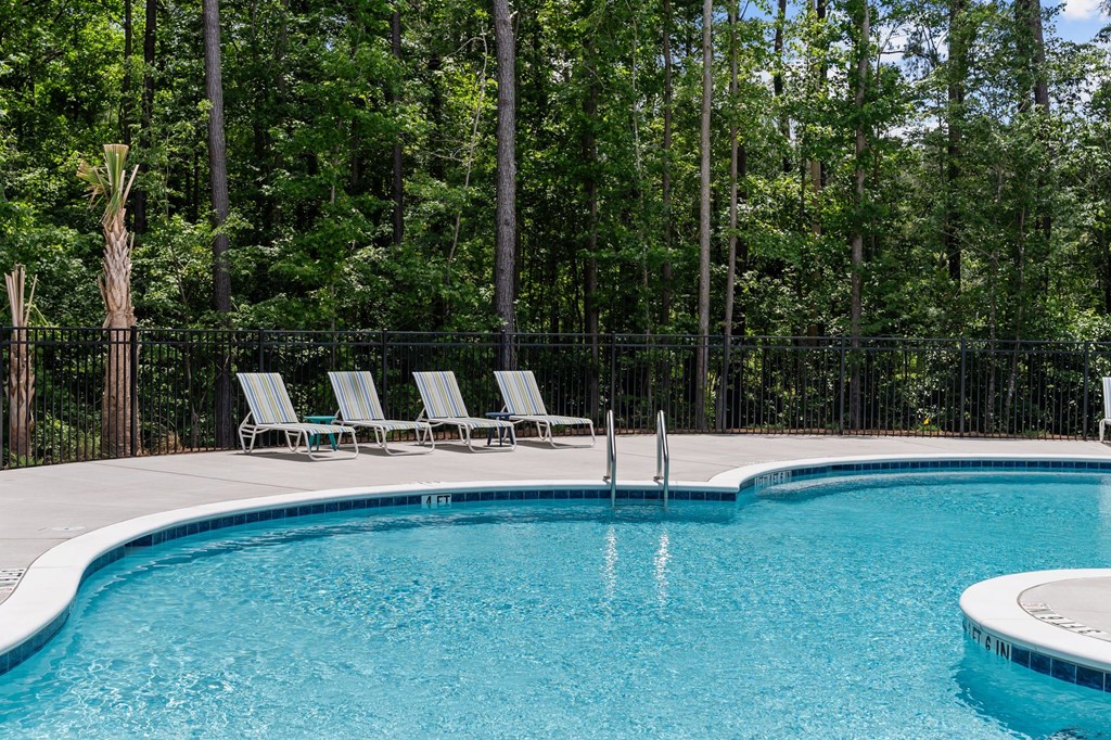A pool surrounded by trees and chairs.