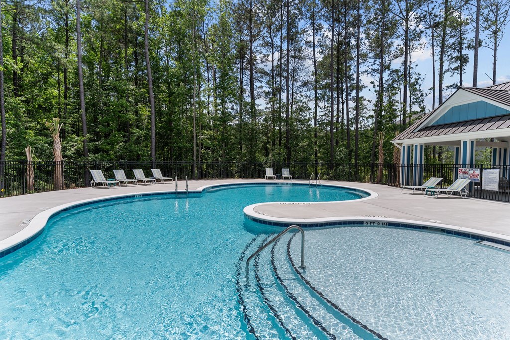 A swimming pool surrounded by trees and lounge chairs.