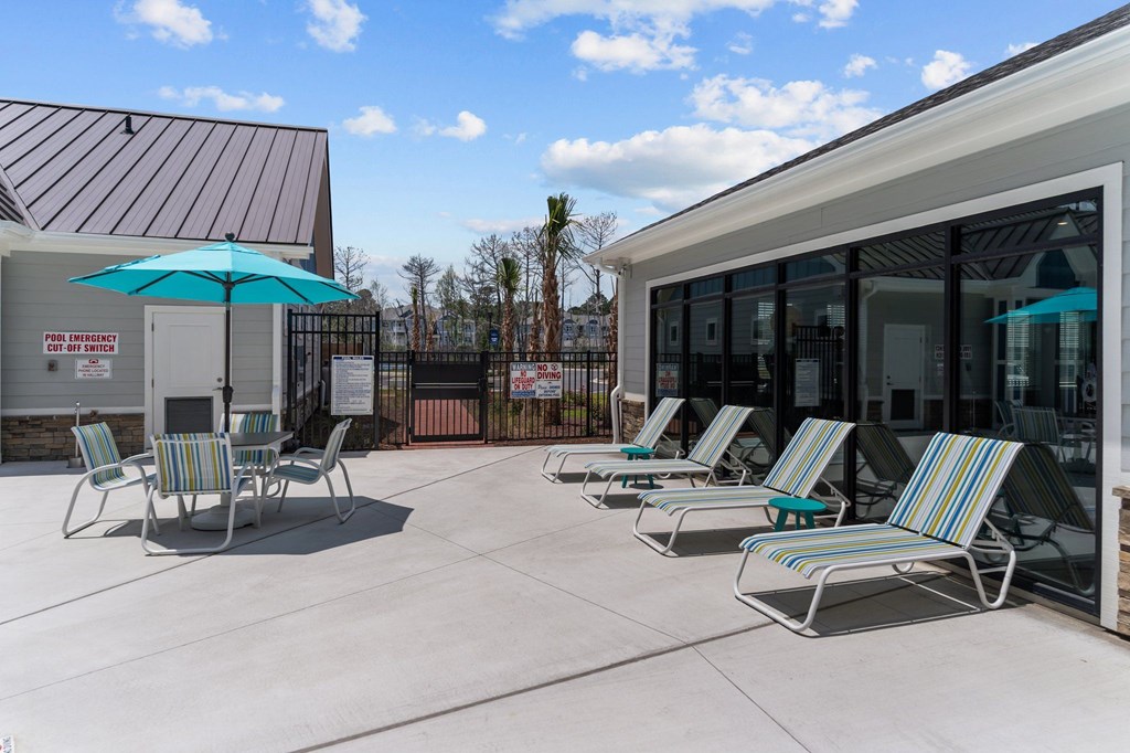 A sunny day at the poolside with chairs and an umbrella.