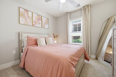 A bedroom with a bed covered in a pink sheet and a ceiling fan.