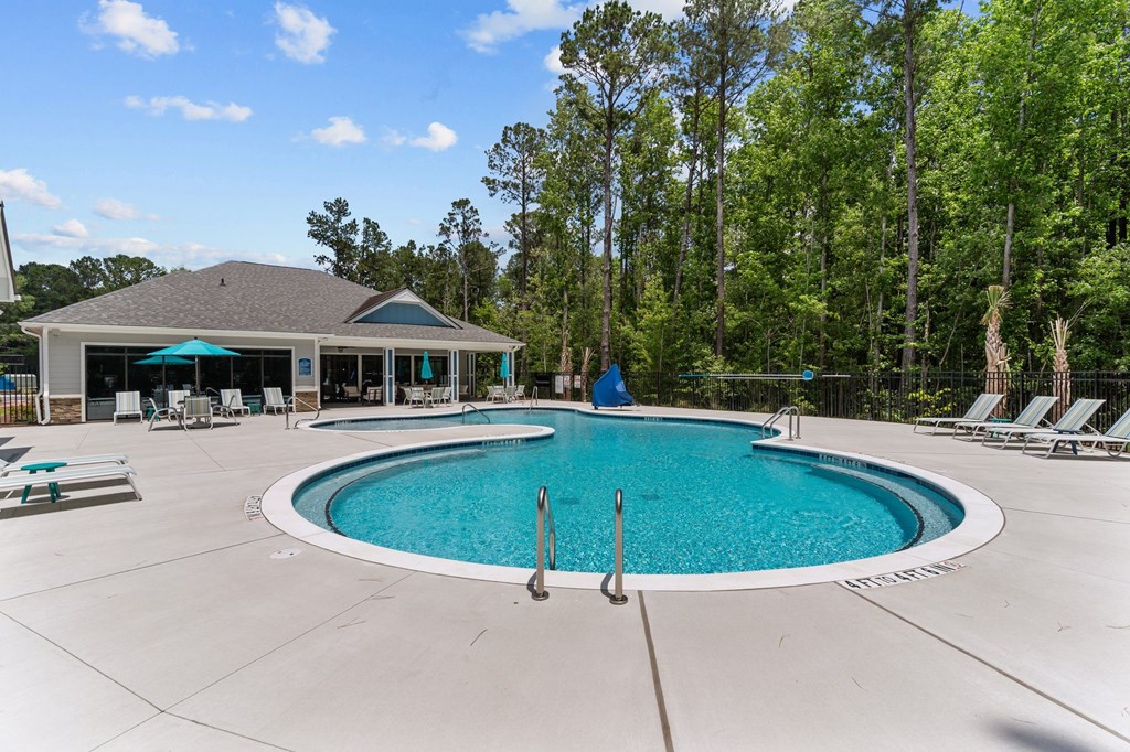 A large outdoor swimming pool with a blue umbrella and a white building in the background.