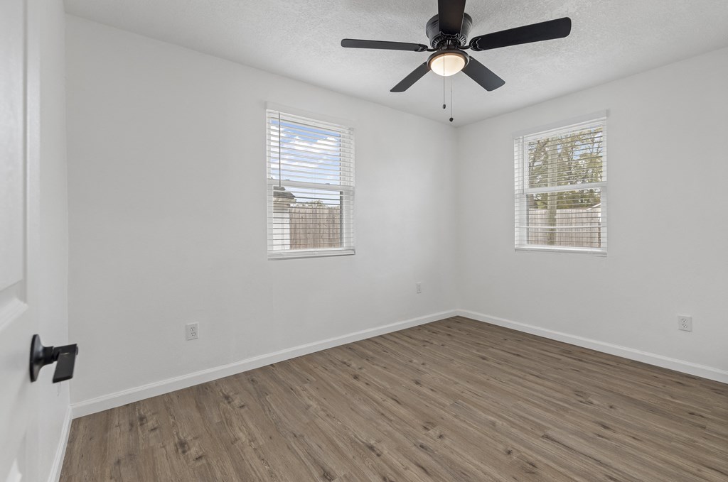 an empty room with a ceiling fan and two windows