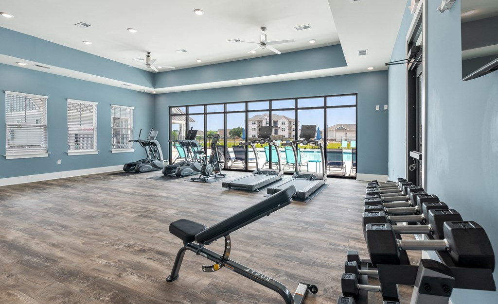 a gym with cardio equipment and a pool in the background
