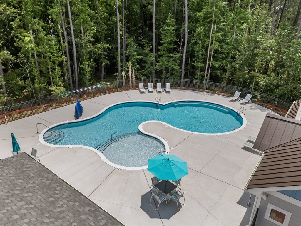 A swimming pool surrounded by trees and deck chairs.