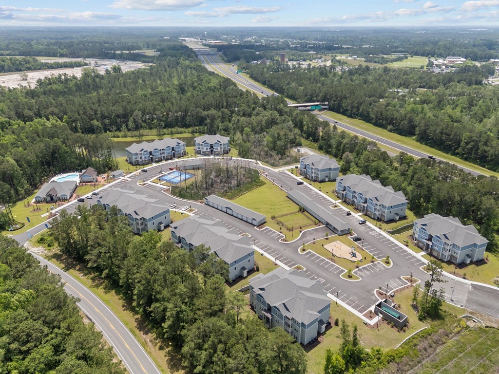 A bird's eye view of a residential complex surrounded by trees and a highway.