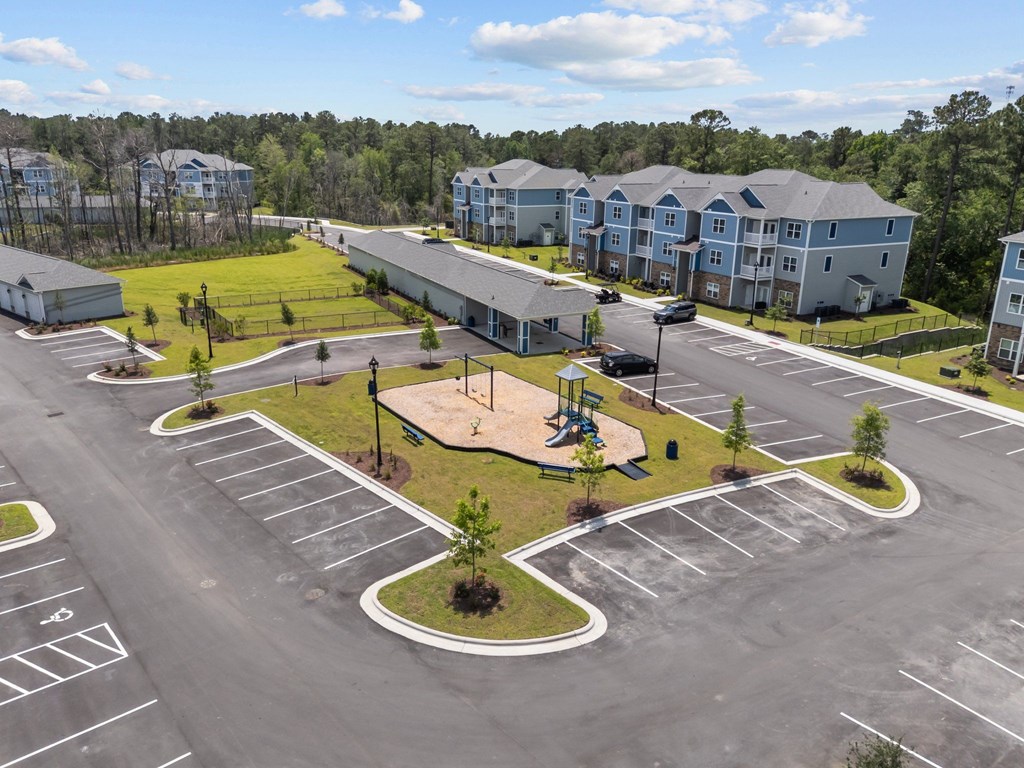 A large parking lot with a playground in the middle and apartment buildings in the background.