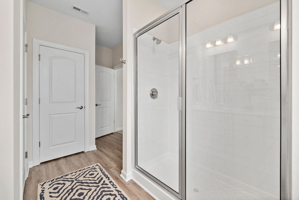 a white bathroom with a glass shower and a rug