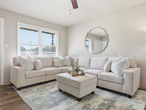 A living room with a white couch and a round mirror on the wall.