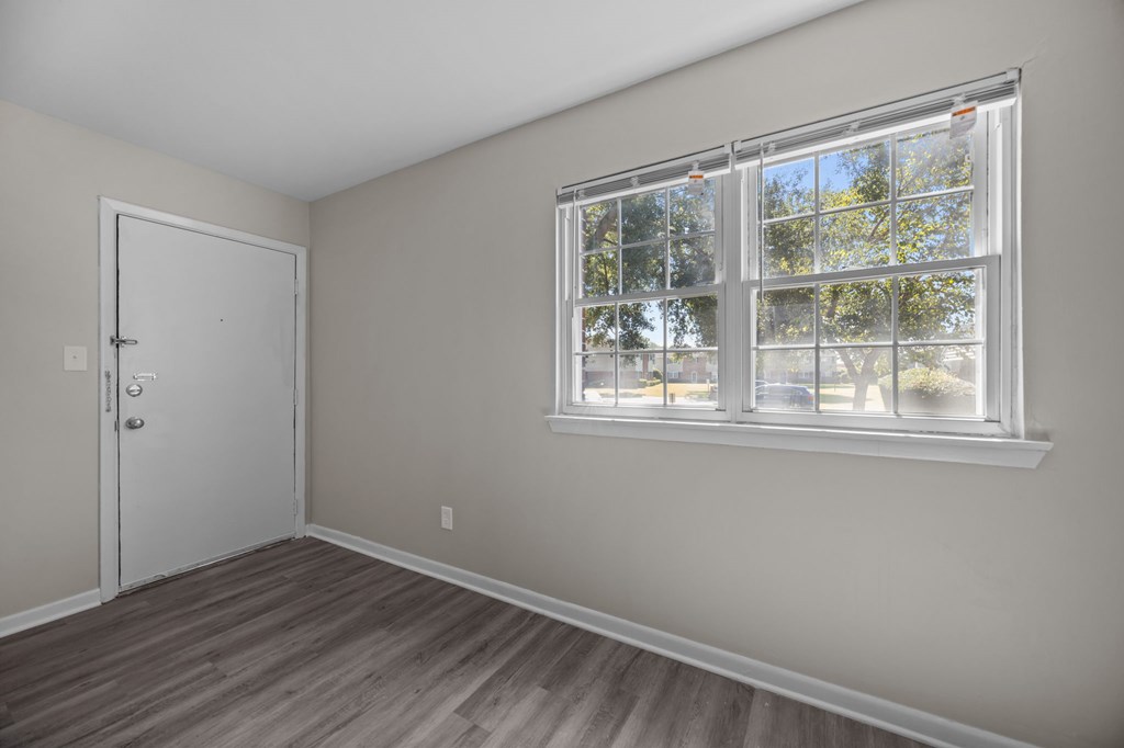 A room with a white door and a window with a view of trees outside.