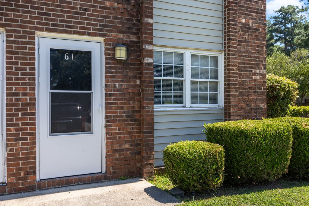 A white door with the number 61 on it is on a brick wall.