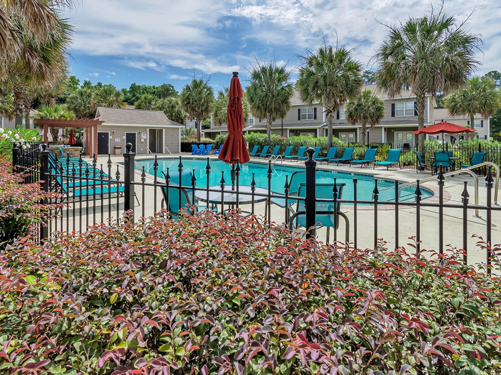 A pool surrounded by red umbrellas and green chairs.