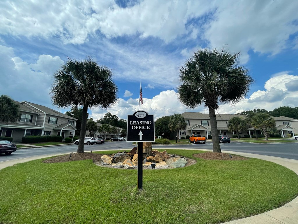 A sign for a leasing office is in the foreground of a residential street.