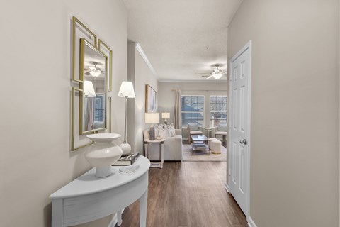 A well-lit, spacious living room with a white sofa set and a large mirror on the wall.