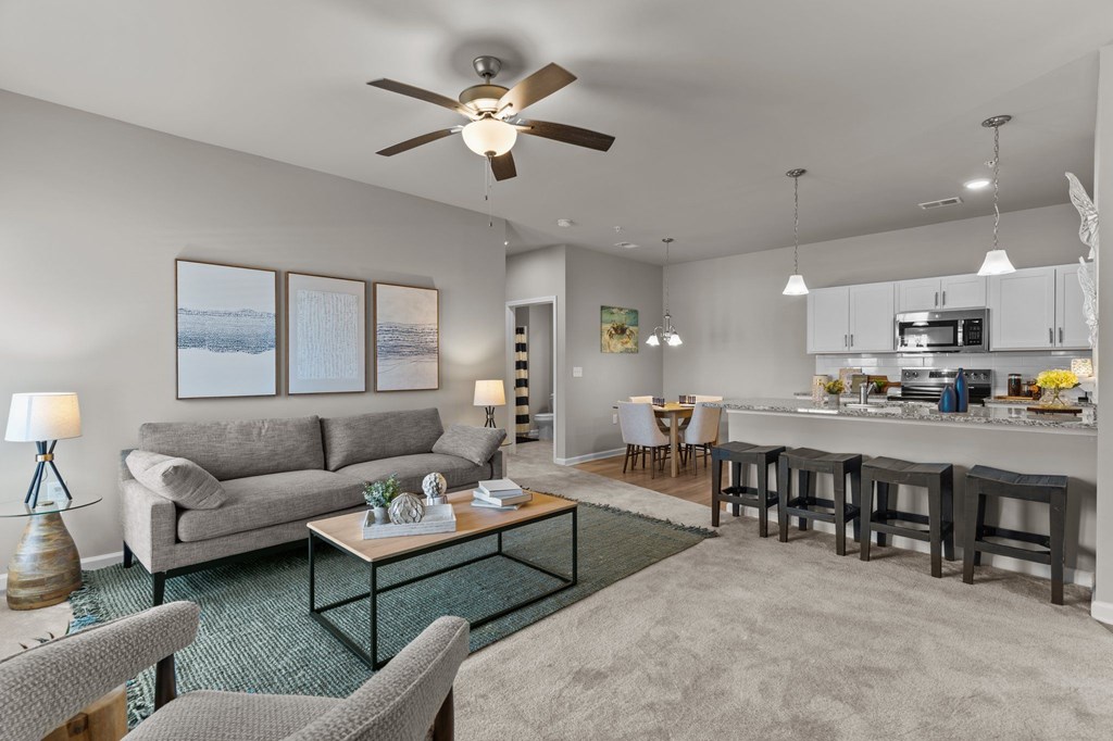 A living room with a grey couch, a glass coffee table, and a ceiling fan.