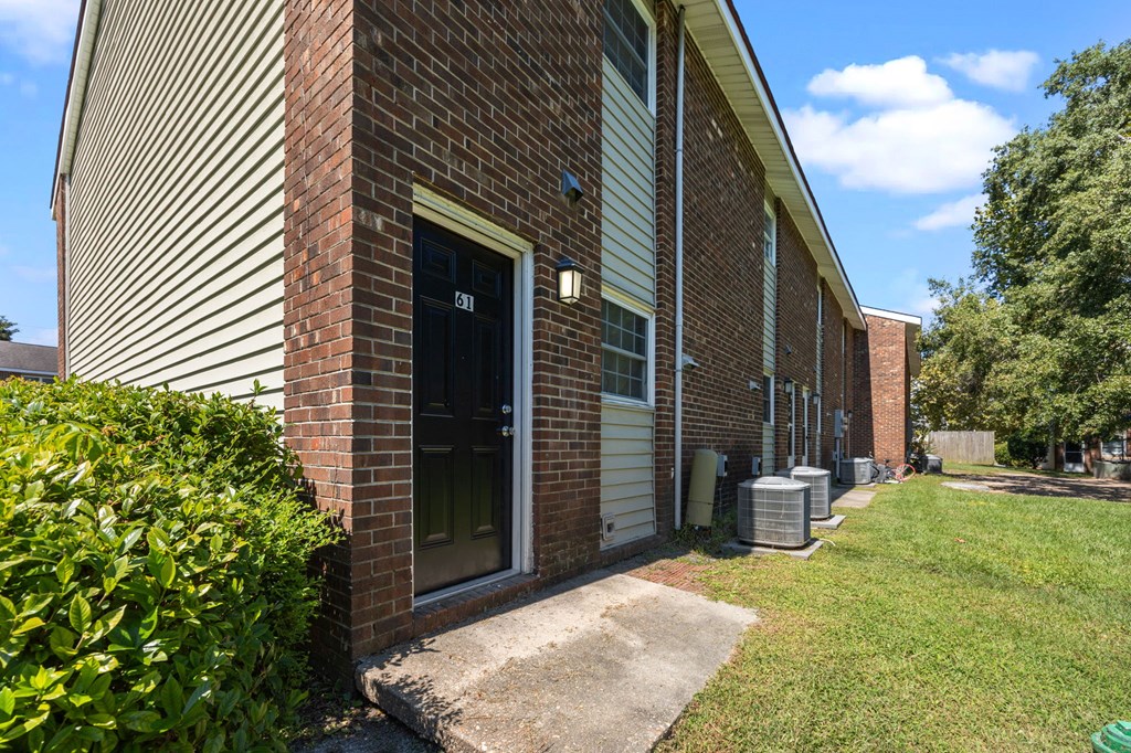 A brick building with a black door and a green bush to the left.