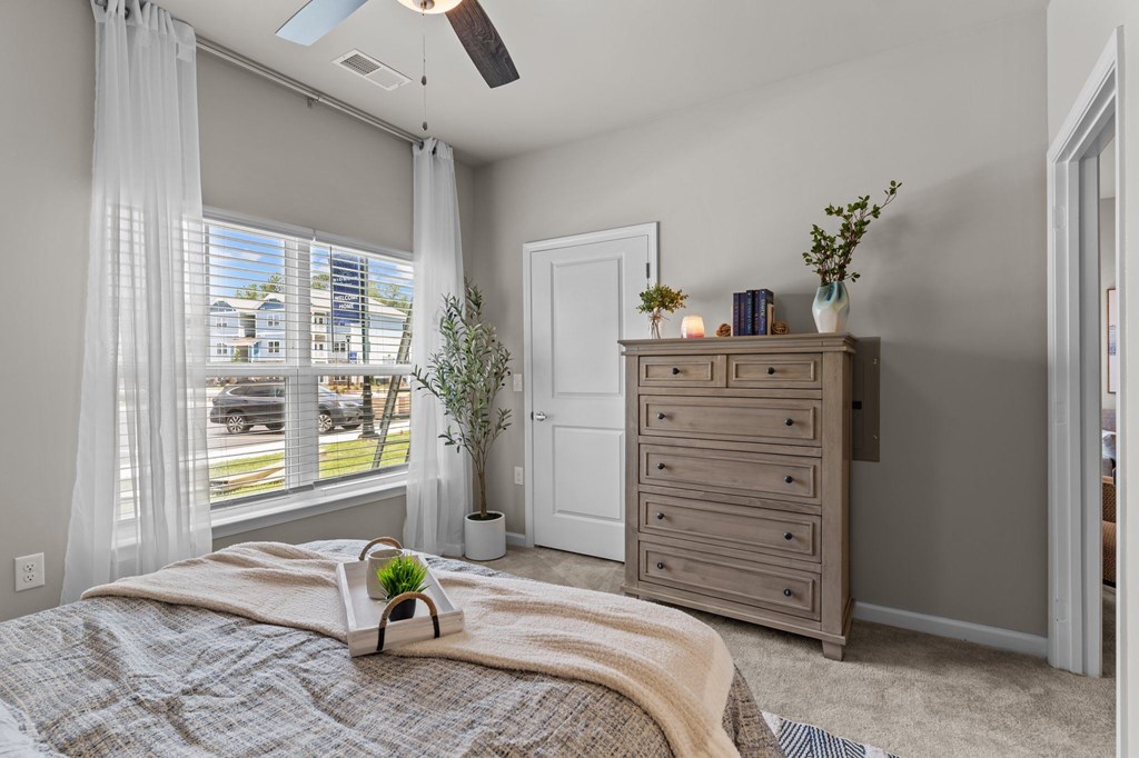 A bedroom with a bed, dresser, and window with curtains.