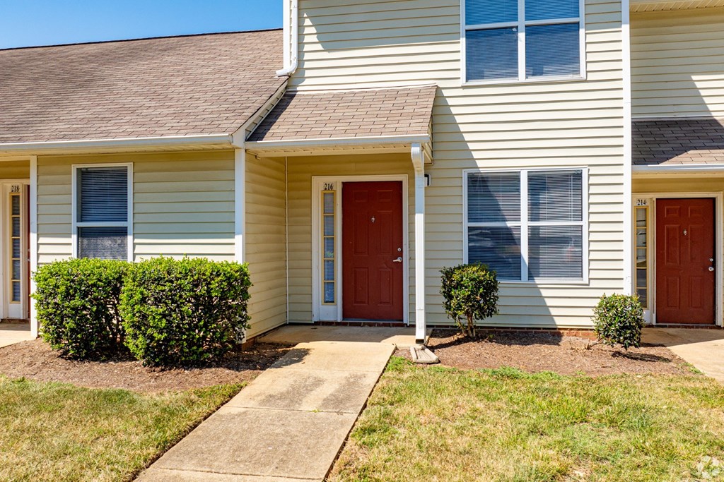 A two-story house with a red door and a small front yard.