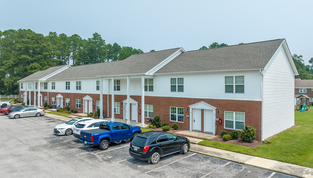 a parking lot in front of a white building with cars parked in front