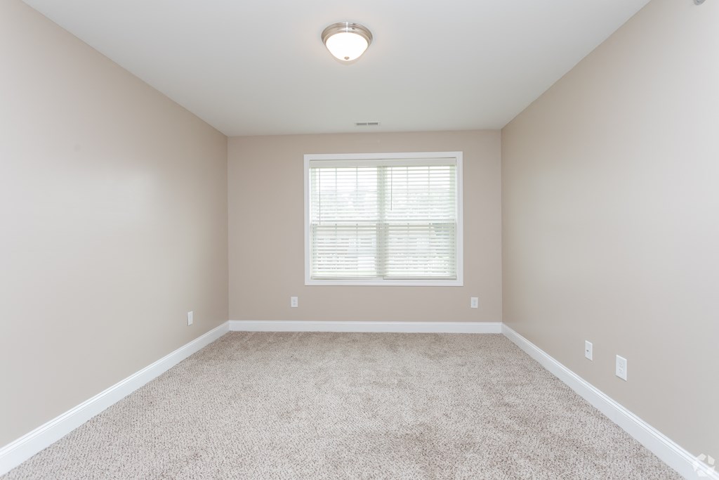 A room with a carpeted floor and a window with blinds.
