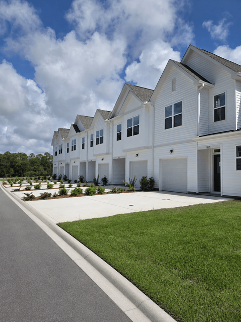 A row of white houses with green lawns in front.
