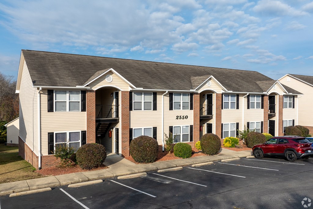 A red car is parked in the parking lot of a building with the number 2550 on it.