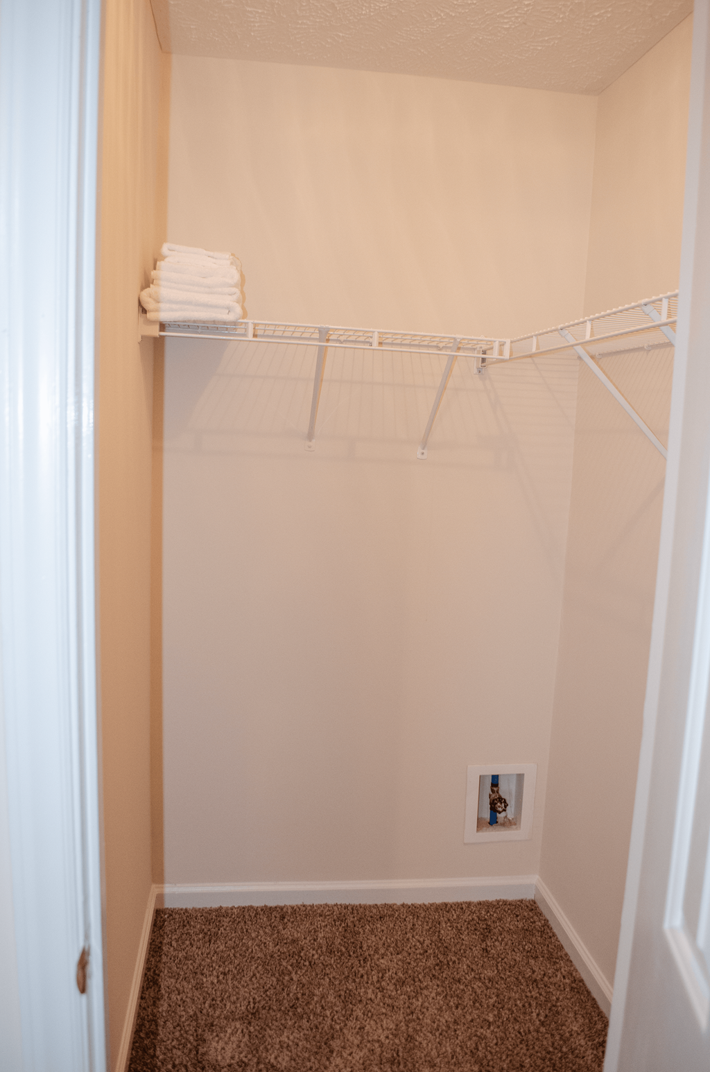 a walk in closet in a small bathroom with white shelves and a rack with towels