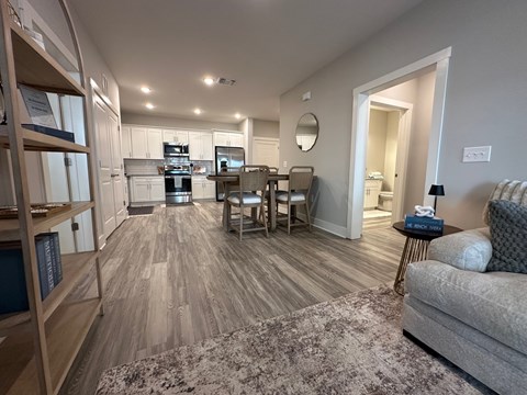 A well-lit, spacious living room with a grey sofa and a wooden bookshelf.