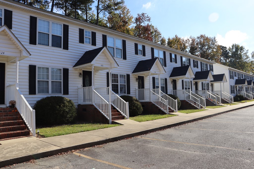a row of white houses with black shutters and a sidewalk