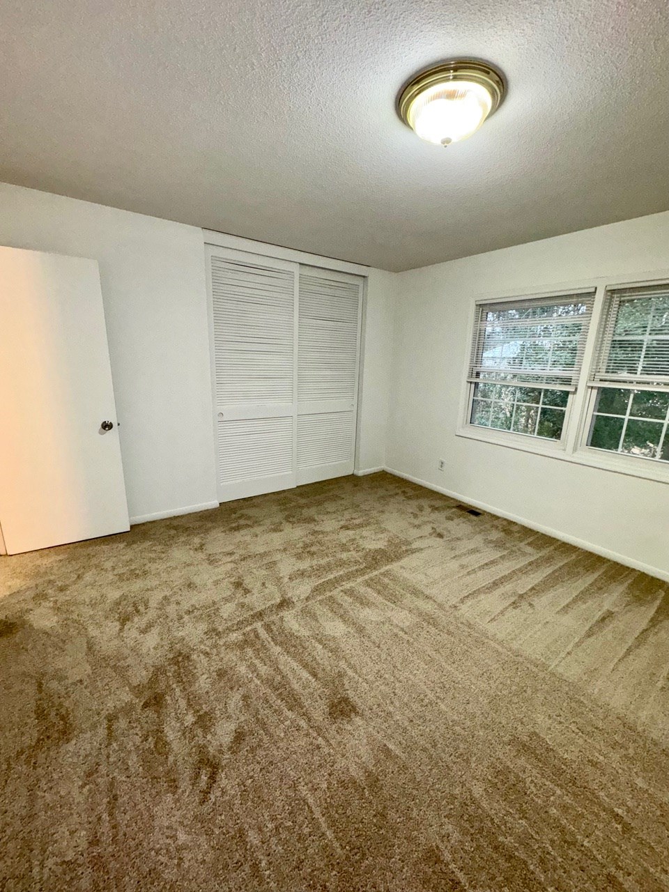 A room with a carpeted floor and a window with blinds.