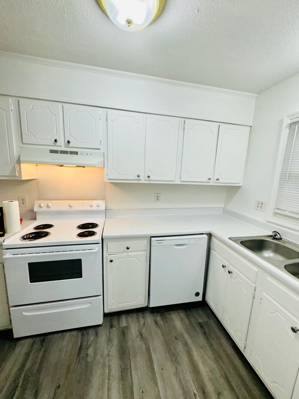 A white kitchen with a stove, dishwasher, and sink.