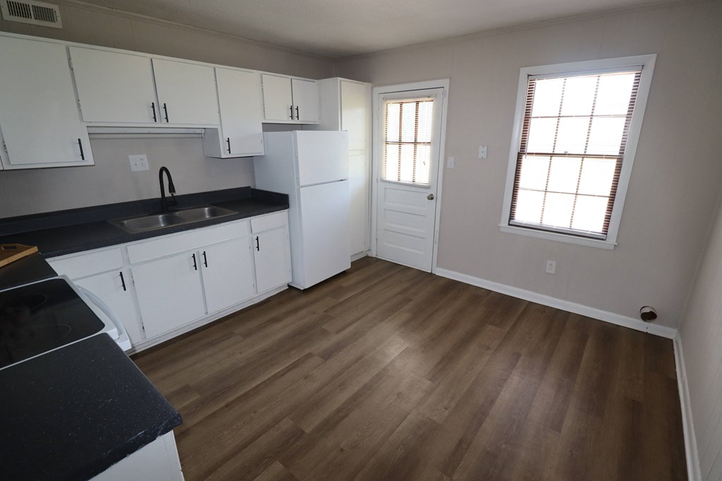 an empty kitchen with white cabinets and wood floors