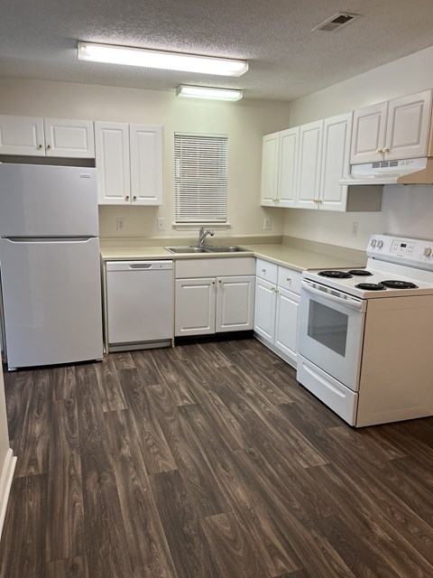 A kitchen with white appliances and wooden floors.