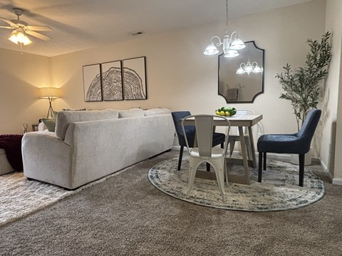 A living room with a grey couch, a small table with chairs, and a rug on the floor.