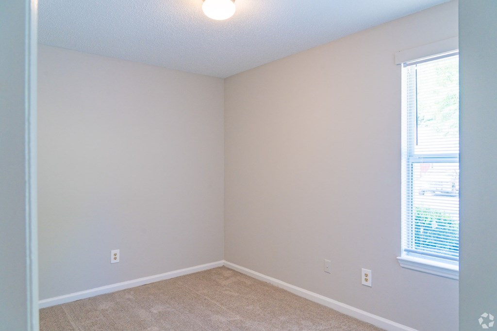 A room with a window and a carpeted floor.