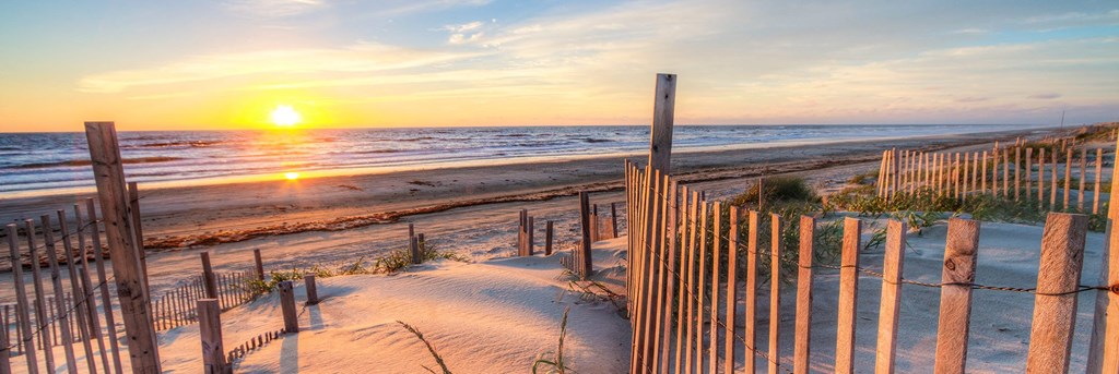 a sunset over the beach and a wooden fence