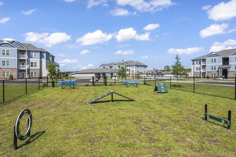 A playground with a slide, swings, and a seesaw in the foreground with apartment buildings in the background.