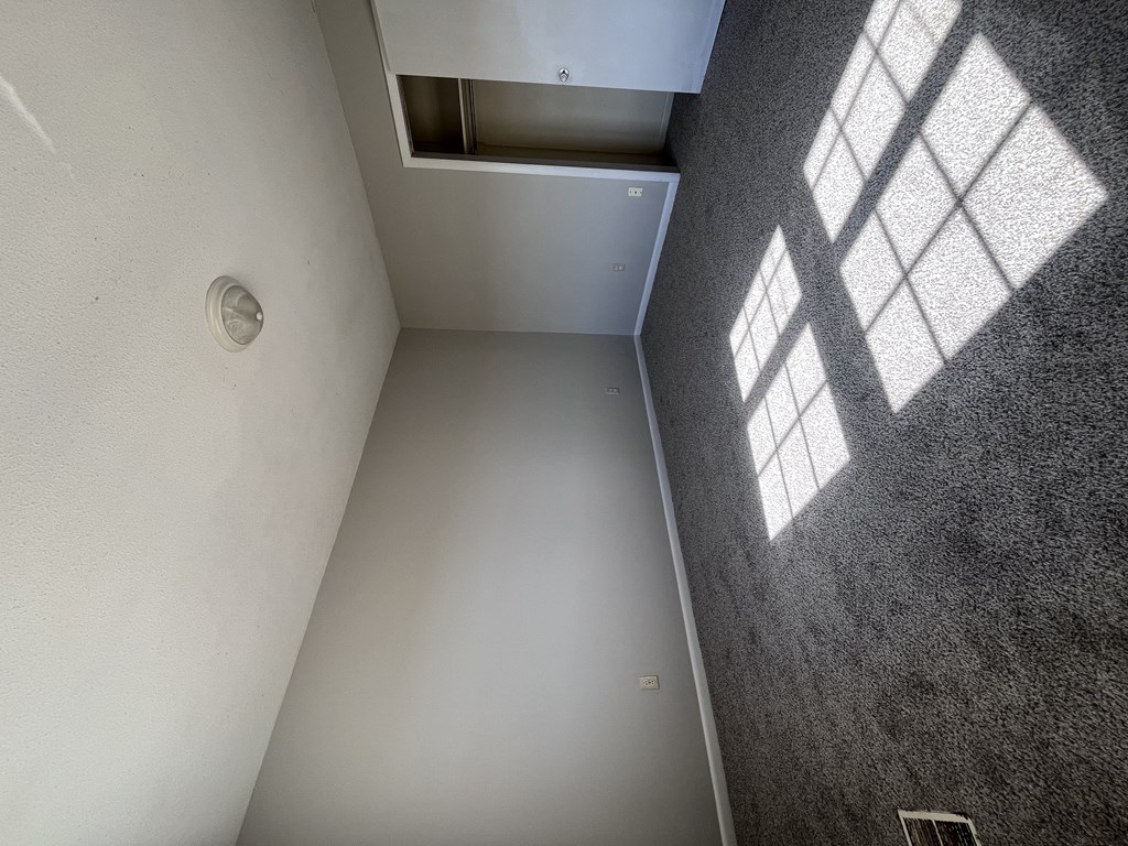 A white wall with a vent and a window casting a shadow on the wall.