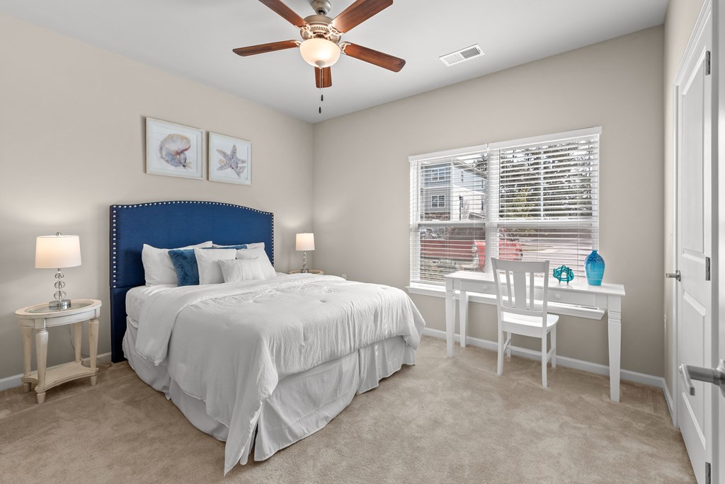 a bedroom with a bed and a desk with a ceiling fan
