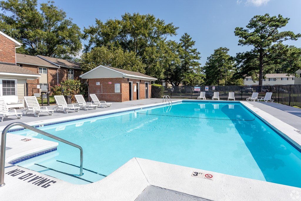 A swimming pool with a diving board and lounge chairs.
