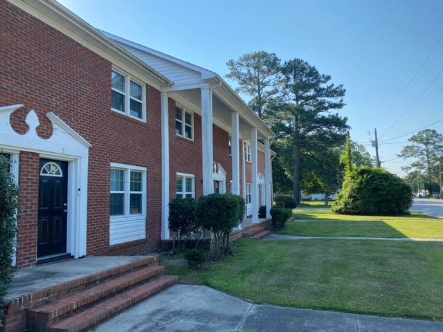 the front of a brick building with steps and a lawn