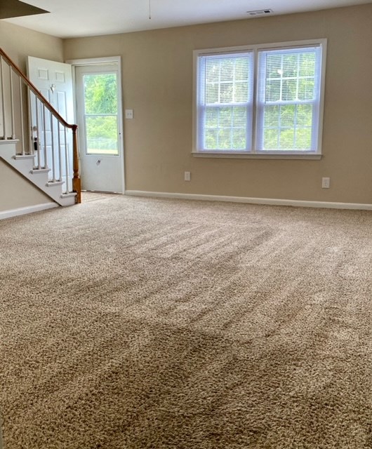 an empty living room with a carpeted floor and a staircase