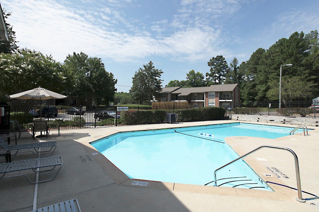 a swimming pool with chairs and umbrellas in front of a building with trees