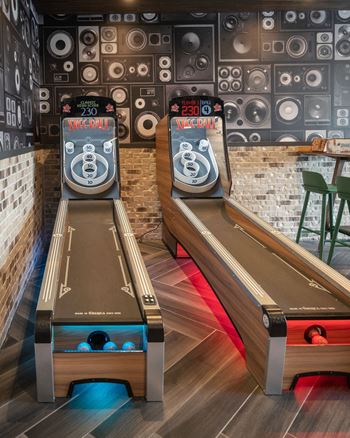 a game room with two shuffleboard tables and a pair of bowling pins on the wall
