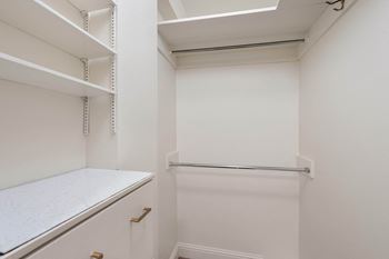 a white walk in closet with shelves and a counter