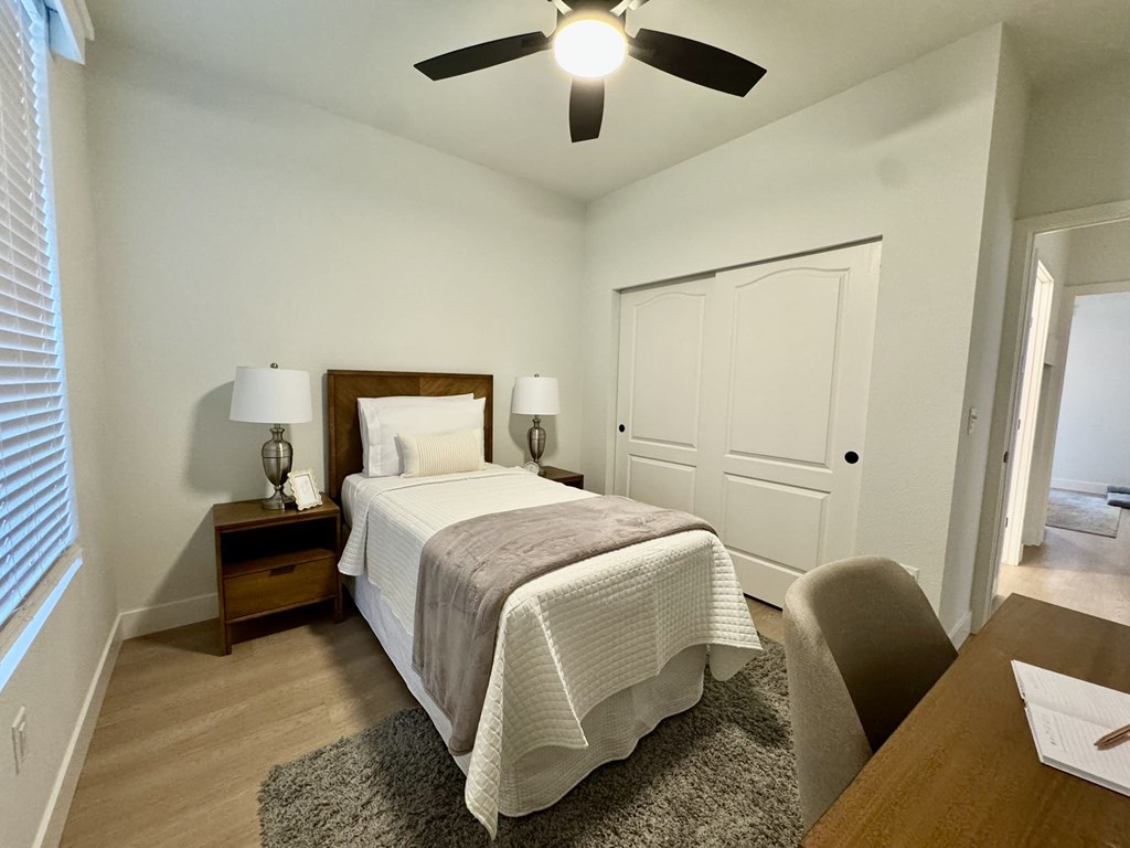 A bedroom with a bed, a chair, and a ceiling fan.