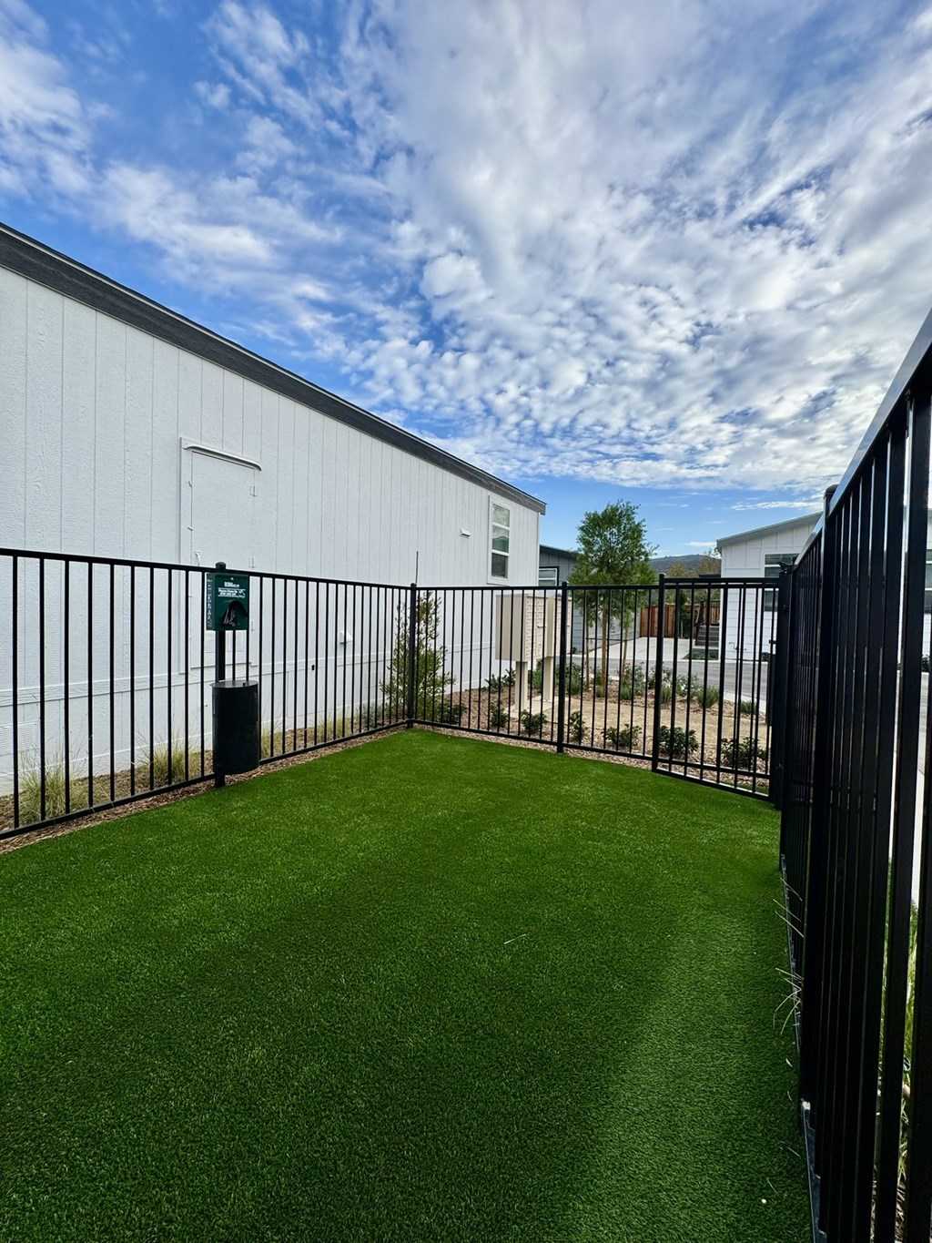 A green lawn in front of a white building with a black fence.