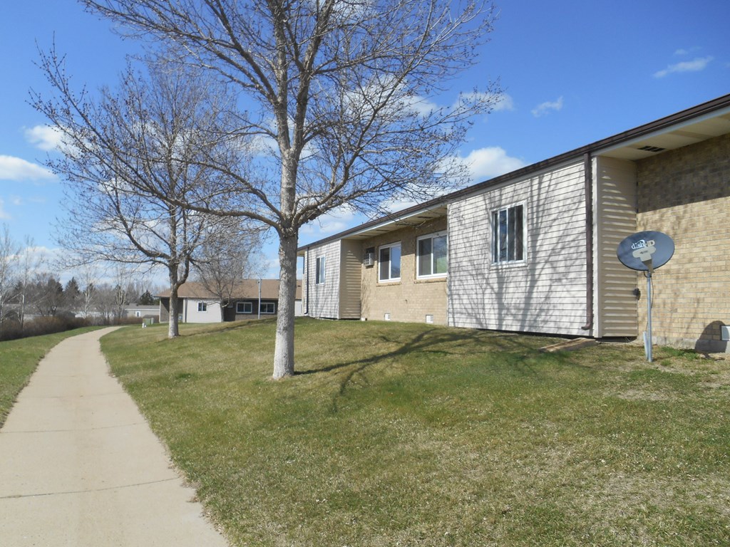 A grassy area in front of a building with a tree and a satellite dish.